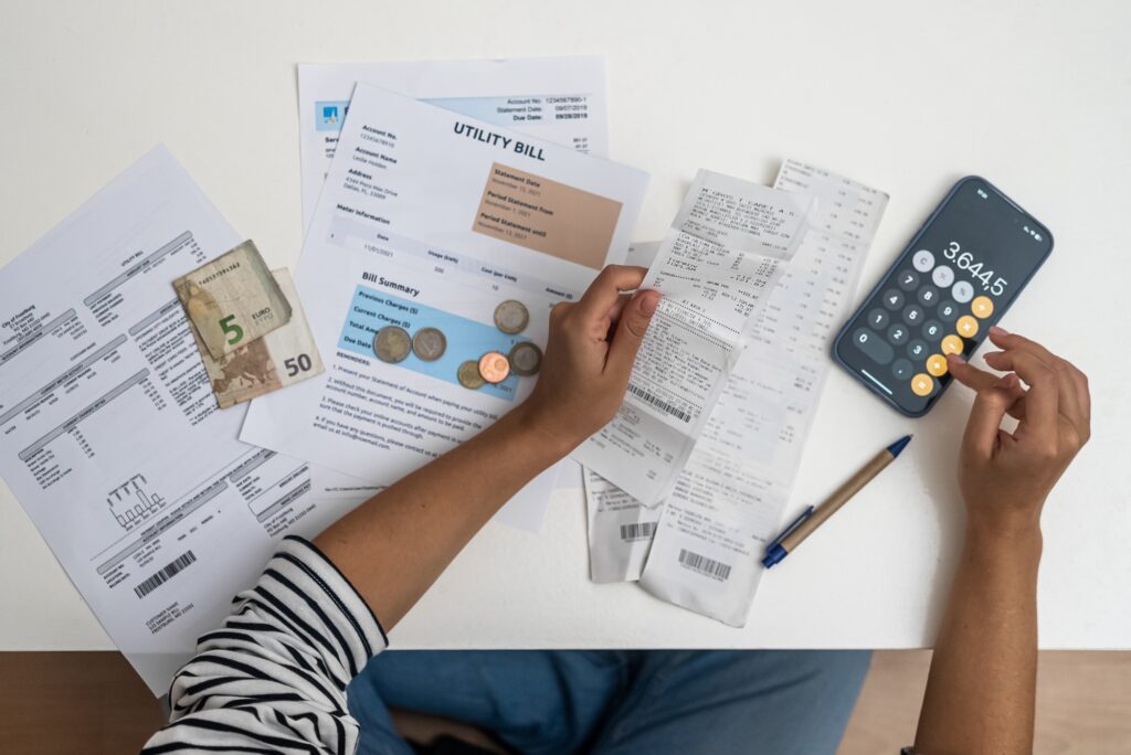 woman carefully assesses utility and bank bills, aided by a smartphone calculator and documents.