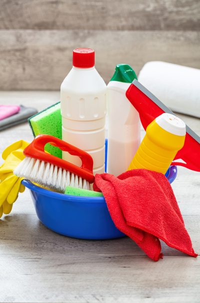 Cleaning supplies in a blue bowl, wooden floor background.